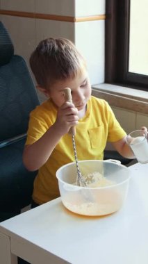 Çocuk elma suyu malzemelerini karıştırıyor, beyaz bir masada oturuyor.