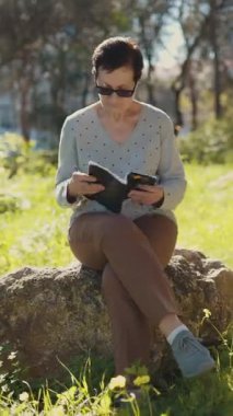 Sunny Park 'ta bir kayanın üzerinde otururken not defterine yazmaktan zevk alan son sınıf öğrencisi kadın.