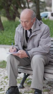 Kıdemli adam bir bankta otururken defterine not alıyor.