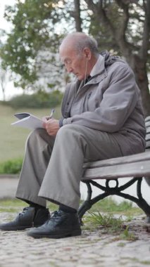 Kıdemli adam bir bankta otururken not defterine not alıyor.