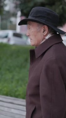 Şapka ve ceket giyen son sınıf öğrencisi parktaki ahşap bir bankta oturuyor.