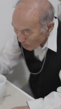 Kıdemli adam bir masada oturmuş, çay ve bisküvilerin tadını çıkarıyor.