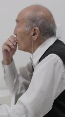 İşitme cihazlı kıdemli adam huzur dolu bir kahvaltıyı seviyor, küçük lokmalar yiyip kahvenin tadını çıkarıyor.