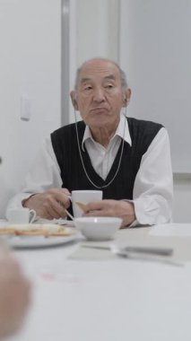 Evde kahvaltıda işitme cihazlı kıdemli adam konuşuyor.