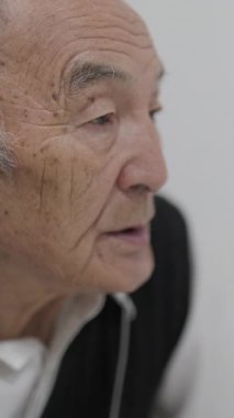 Kulaklık takan kıdemli adam konuşuyor ve beyaz bir arkaplanda el kol hareketi yapıyor.