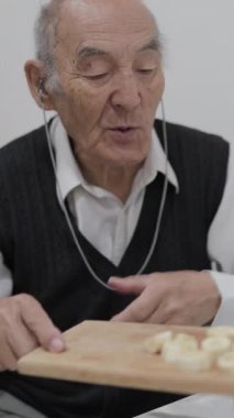 Kıdemli adam kahvaltıda gözlemelere dilimlenmiş muz ekliyor.