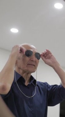 Yaşlı adam dans ediyor ve aynanın önünde güneş gözlüğü takıyor.