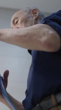 Kıdemli adam mavi kravatı katlarken kulaklıkla müzik dinliyor.