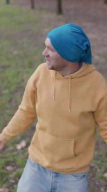 Mavi kapüşonlu ve kot pantolonlu bir erkek dansçı sonbahar parkı ortamında spontane dans hareketi yapıyor. Hafta sonu boş zamanlarında pozitif enerji ve kişisel özgürlük yaymak.