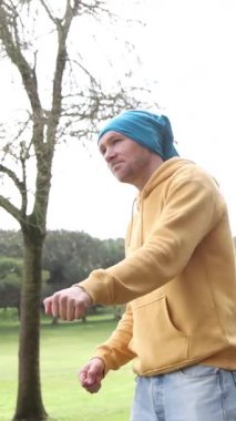 Parkta tek başına dans eden adam sarı kazak giyiyor.