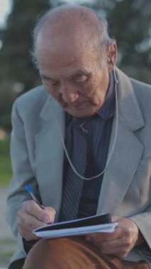 Son sınıf öğrencisi bankta oturuyor, parkta not defterine yazıyor.