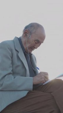 Kıdemli adam bankta oturuyor, deftere yazıyor, parkta huzurlu bir anın tadını çıkarıyor.