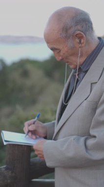 Kıdemli adam deniz kenarındaki defterine not alıyor.