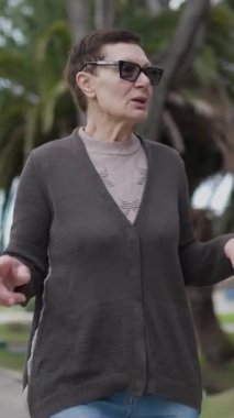 Yaşlı kadın parkta yürürken bir şey anlatıyor.