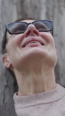 Yaşlı kadın, parkta bir ağacın yanında farklı duygular ve duygular ifade eden gözlük takıyor.