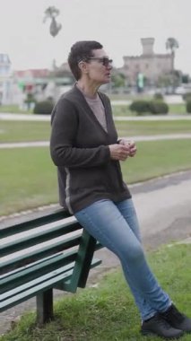 Kadın parkta konuşurken gözlük takıyor ve jestler yapıyor.