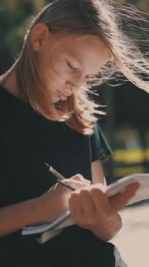 Dışarıda yazan genç bir öğrenci, parkta notlar alan konsantre bir kız.