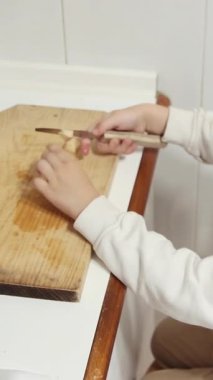 Anaokulu öğrencisi, ahşap tahtada elma parçaları keserek temel yaşam becerilerini geliştirir.