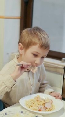 Çocuk makarna ve sosis yemekten zevk alıyor, akvaryumun yanındaki masada oturuyor.