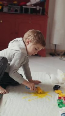 Genç çocuk yaratıcı oyun zamanını seviyor, yere saçılmış kağıtta sarı boya ile resim yapıyor.