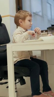 Anaokulu çocuğu modern bir mutfakta tablet izlerken yemeğin tadını çıkarıyor.