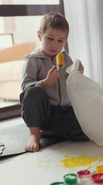 Genç bir çocuk yerdeki plastik bir torbanın içine resim yaparak sanat yapıyor.