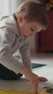 Anaokulu öğrencisi yaratıcı oyun zamanını seviyor, yerde sarı boya ile resim yapıyor.