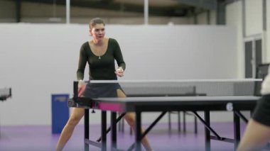 Genç bayan sporcu bir spor salonunda konsantre oluyor ve rekabetçi bir masa tenisi maçı oynuyor.