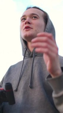 Gri kapüşonlu genç bir adam parkta dürbünle gözetliyor.