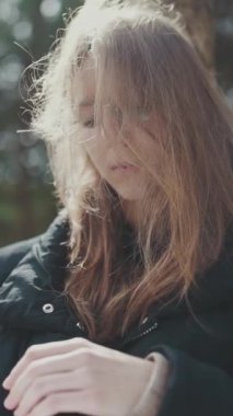 Genç bir öğrenci açık havada kitap okuyor, rüzgarlı bir günde saçını düzeltiyor.