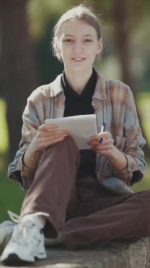 Genç kız parkta oturan bir defterden notlar alıyor.