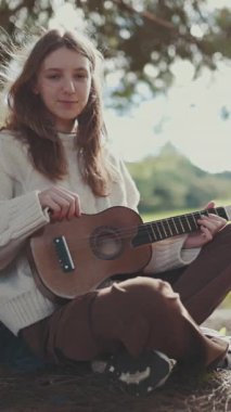 Müzisyen doğada bir ağacın altında ukulele çalışır.
