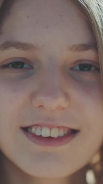 Genç kız gün ışığında sıcak bir şekilde gülümsüyor. Uzun saçlar nazikçe sallanıyor, doğal ve samimi bir ifade sergiliyor. Gençlik masumiyetini ve açık hava atmosferini yakalar.