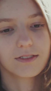 Genç sarışın kadın aşağıya bakıyor, doğasında hafifçe gülümsüyor.