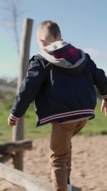 Çocuk ahşap kiriş üzerinde dikkatle yürüyor, dengeyi sağlıyor ve dışarıda oynamaktan zevk alıyor.