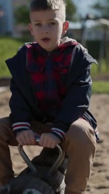 Çocuk parkta tahta bir sallanan ata binerken eğleniyor.