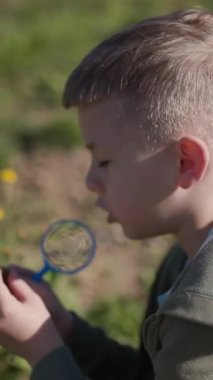 Küçük çocuk sarı çiçekleri büyüteçle inceliyor, güneşli parkta doğayı keşfediyor.