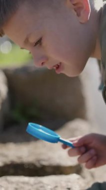 Genç çocuk büyüteçle doğayı araştırıyor, çevrelerinde harikalar keşfediyor.