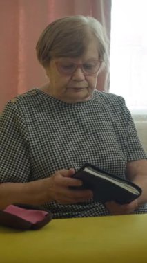 Sarı bir kanepede oturan yaşlı kadın kapıyı açar ve bir kitap okur.