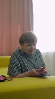 Üst düzey bir kadın oturma odasındaki bir kanepede otururken akıllı telefonuyla konuşuyor.