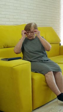 Senior woman relaxing on a yellow sofa, reading a book in her living room