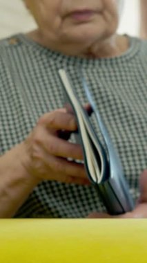 Yaşlı kadın rahat sarı bir kanepede dinleniyor, kitaptan zevk alıyor ve gözlüklerini çıkarıyor.