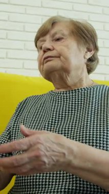 Üst düzey kadın uzaktan kumanda kullanıyor, sarı kanepeden televizyon kanallarında geziniyor.