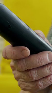 Uzaktan kumandayı elinde tutan, televizyon izleyen, sarı koltukta oturan yaşlı bir kadın.