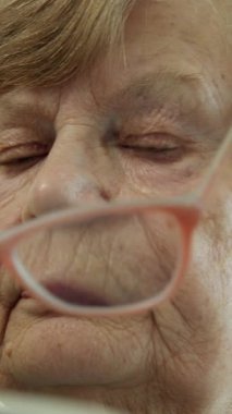 Kıdemli kadın kitap okuyor, görüşünü geliştirmek için gözlüklerini ayarlıyor.