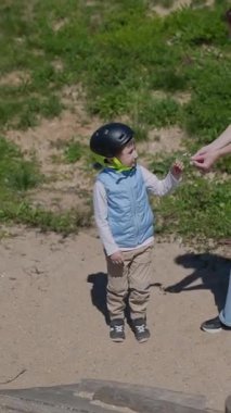 Kask takan bir çocuk annesiyle oyun bahçesinde kumla oynuyor.