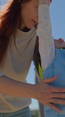 Anne, oğlunun oyun parkında oynarken kaskını ve yeleğini giyiyor.