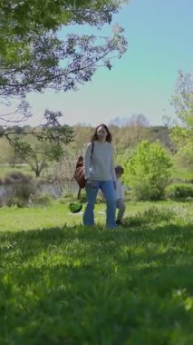 Anne ve oğlu güneşli bir günde göl kenarındaki kazların yanında parkta yürüyüş yapıyorlar.