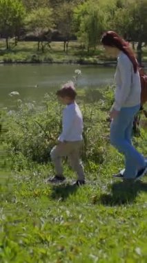 Anne ve oğlu güneşli bir günde göl kenarında keyifli bir yürüyüş yapıyorlar.