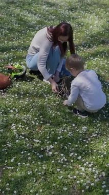 Anne ve oğul küçük beyaz çiçeklerle dolu bir tarlada çiçek topluyor.